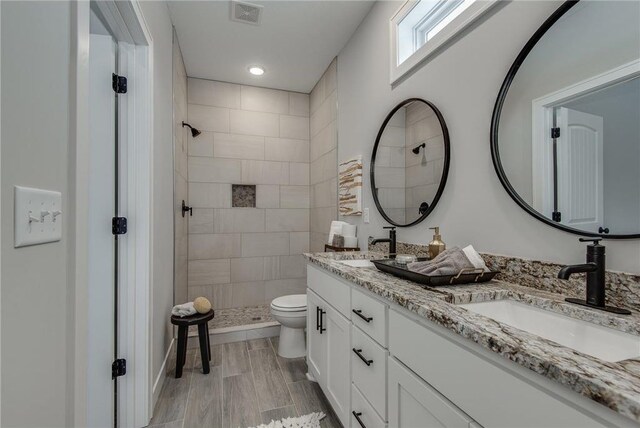 bathroom with a tile shower, toilet, vanity, and hardwood / wood-style flooring