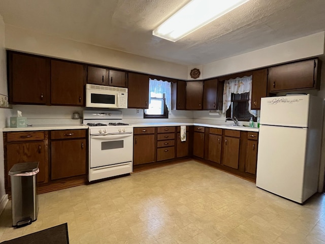 kitchen with sink, dark brown cabinetry, white appliances, and a textured ceiling