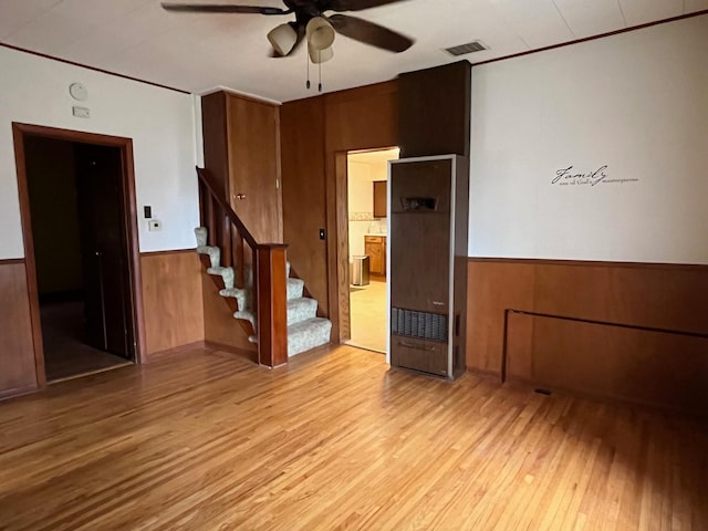 empty room featuring light wood-type flooring, ceiling fan, and wooden walls