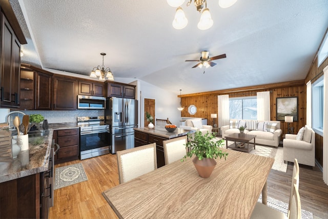 kitchen featuring hanging light fixtures, appliances with stainless steel finishes, wooden walls, and dark brown cabinets