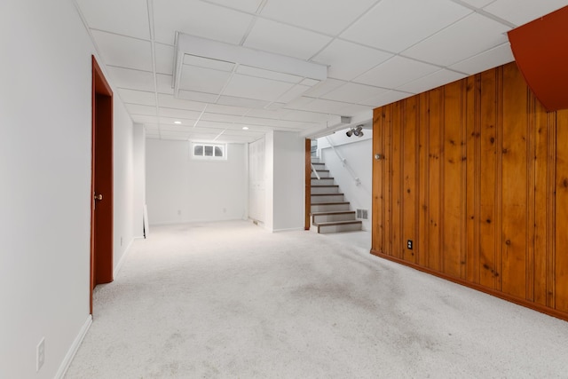 basement featuring wood walls, a drop ceiling, and light colored carpet