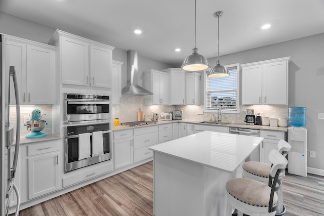 kitchen with white cabinets, a center island, appliances with stainless steel finishes, wall chimney range hood, and sink