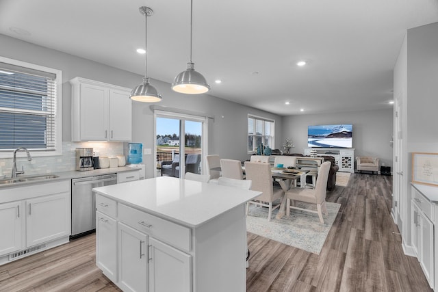 kitchen featuring white cabinets, sink, backsplash, hanging light fixtures, and stainless steel dishwasher