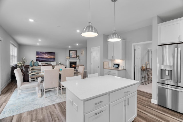 kitchen featuring white cabinets, a center island, decorative light fixtures, stainless steel fridge with ice dispenser, and light hardwood / wood-style flooring