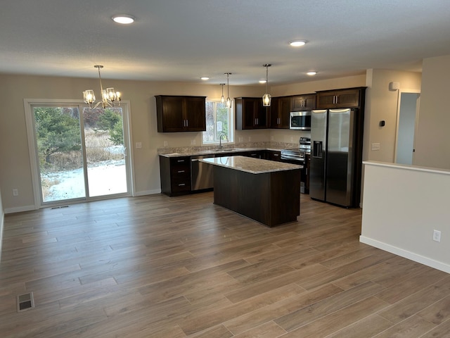 kitchen with appliances with stainless steel finishes, dark brown cabinetry, decorative light fixtures, light hardwood / wood-style flooring, and a kitchen island