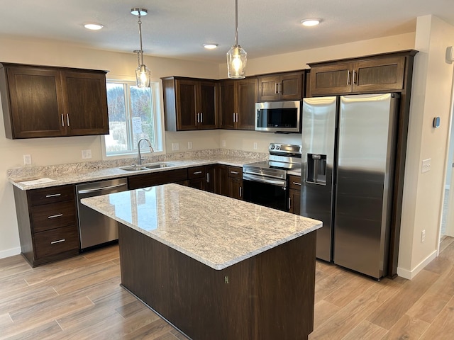 kitchen with sink, stainless steel appliances, pendant lighting, a kitchen island, and light wood-type flooring