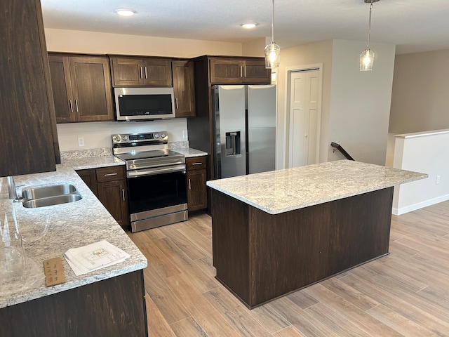 kitchen with light stone countertops, light wood-type flooring, stainless steel appliances, and hanging light fixtures