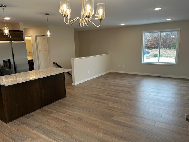 kitchen featuring pendant lighting, hardwood / wood-style floors, an inviting chandelier, light stone counters, and dark brown cabinetry