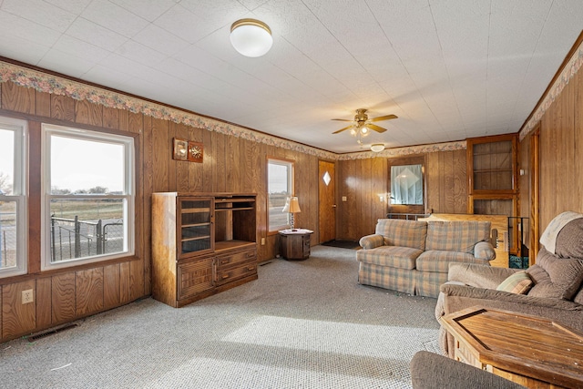 carpeted living room featuring ceiling fan, wood walls, and a wealth of natural light