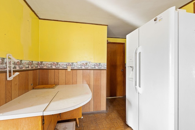 kitchen with dark parquet floors, white fridge with ice dispenser, and wood walls