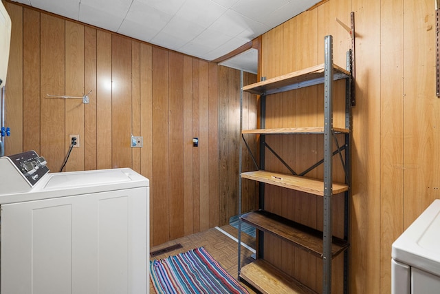 clothes washing area featuring wood walls, light parquet flooring, and washer and dryer