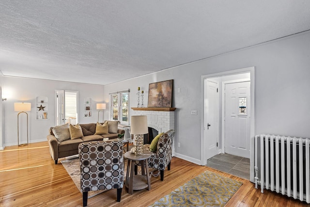 living room featuring radiator, wood-type flooring, a textured ceiling, and a brick fireplace