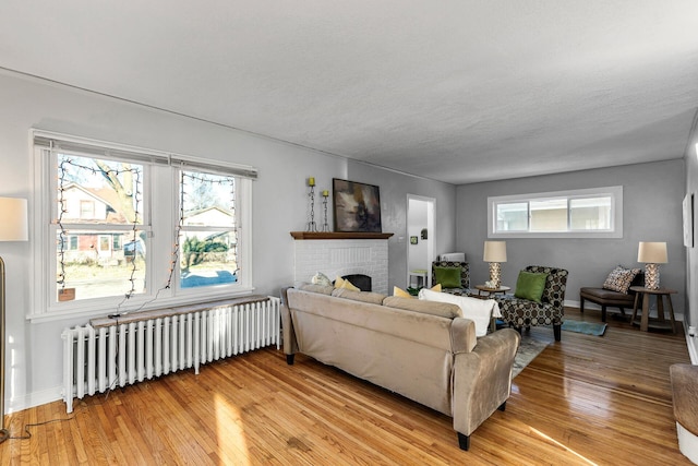 living room featuring a brick fireplace, a textured ceiling, light hardwood / wood-style flooring, and radiator