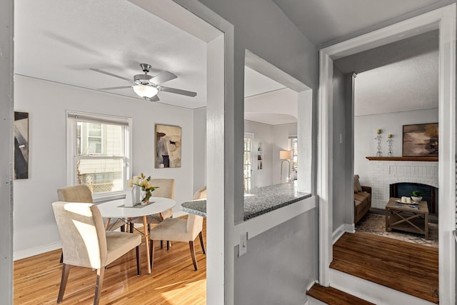 dining area featuring ceiling fan, wood-type flooring, and a brick fireplace