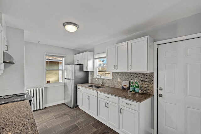 kitchen with radiator, sink, dark hardwood / wood-style floors, dark stone countertops, and white cabinetry