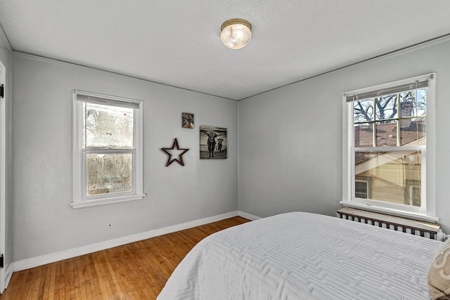 bedroom with crown molding, wood-type flooring, a textured ceiling, and multiple windows