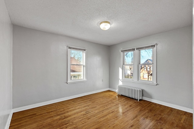 empty room with hardwood / wood-style floors, a textured ceiling, and radiator