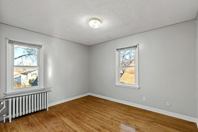 empty room with hardwood / wood-style flooring, a wealth of natural light, a textured ceiling, and radiator