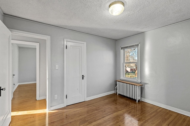 empty room featuring radiator heating unit, a textured ceiling, and hardwood / wood-style flooring