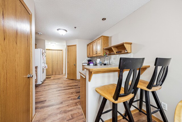 kitchen with backsplash, a kitchen breakfast bar, white refrigerator, light wood-type flooring, and a textured ceiling