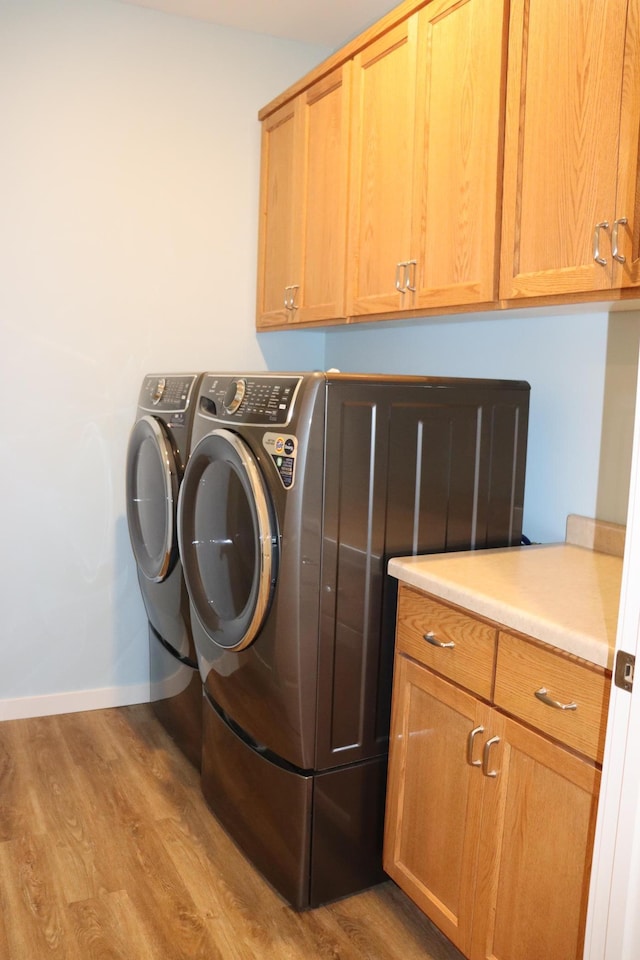 washroom featuring washing machine and clothes dryer, cabinets, and light wood-type flooring