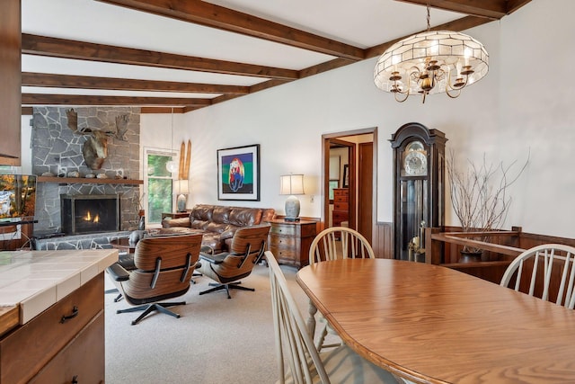 dining space with carpet flooring, a stone fireplace, beamed ceiling, and an inviting chandelier