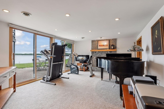 interior space featuring carpet floors, a water view, a stone fireplace, and expansive windows