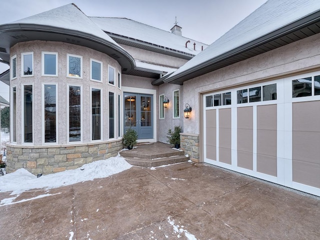 doorway to property featuring an attached garage, stucco siding, stone siding, and french doors