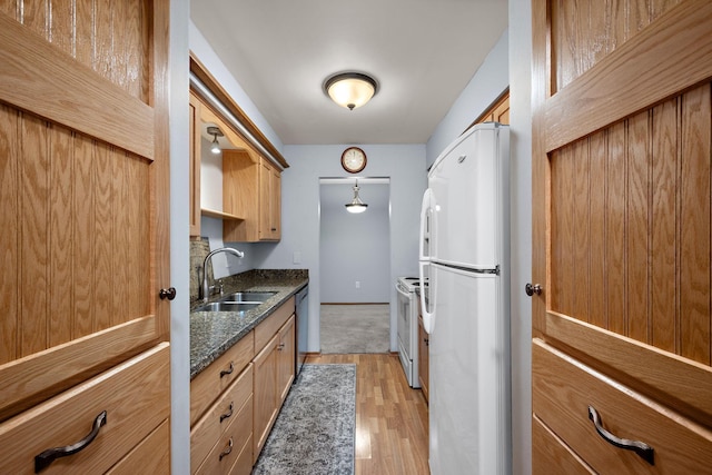 kitchen with light wood-type flooring, white appliances, dark stone counters, and sink