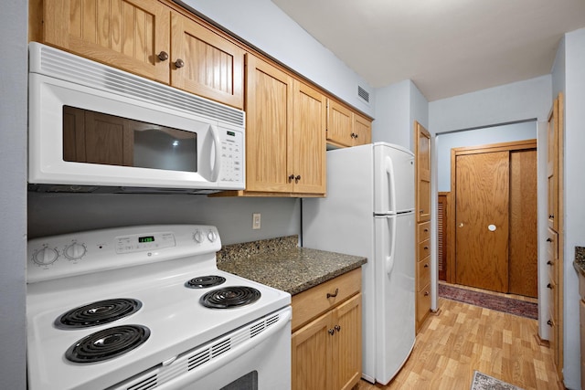 kitchen with light wood-type flooring, light brown cabinets, white appliances, and dark stone countertops