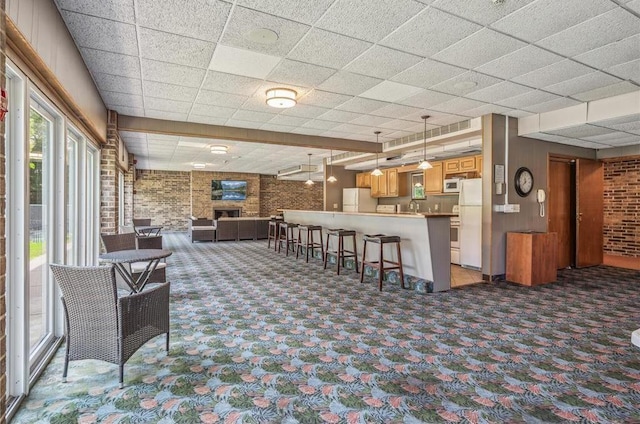 interior space featuring a stone fireplace, a paneled ceiling, carpet floors, and brick wall