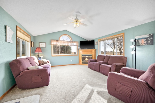 carpeted living area with lofted ceiling, plenty of natural light, a glass covered fireplace, and baseboards