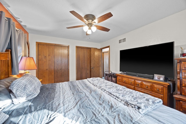 bedroom with a ceiling fan, visible vents, a textured ceiling, and two closets