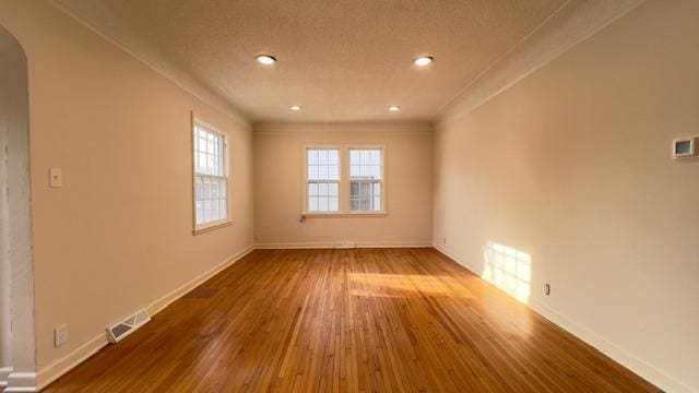 empty room with a textured ceiling, wood-type flooring, and crown molding