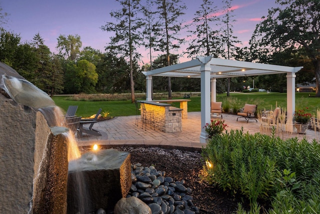 patio terrace at dusk featuring an outdoor bar and a lawn