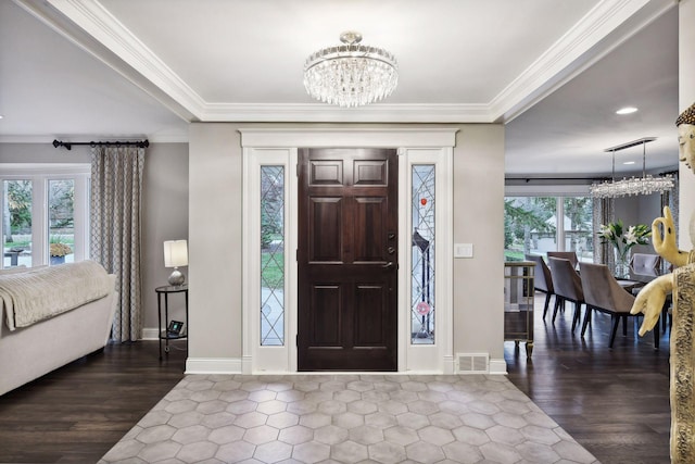 foyer entrance with dark wood-type flooring, ornamental molding, and a notable chandelier