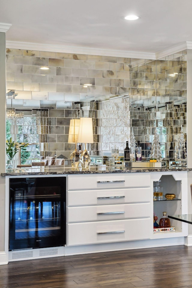 bar featuring crown molding, dark wood-type flooring, white cabinets, beverage cooler, and dark stone counters