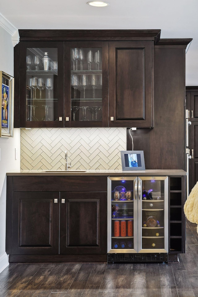 bar featuring crown molding, sink, beverage cooler, and dark brown cabinetry