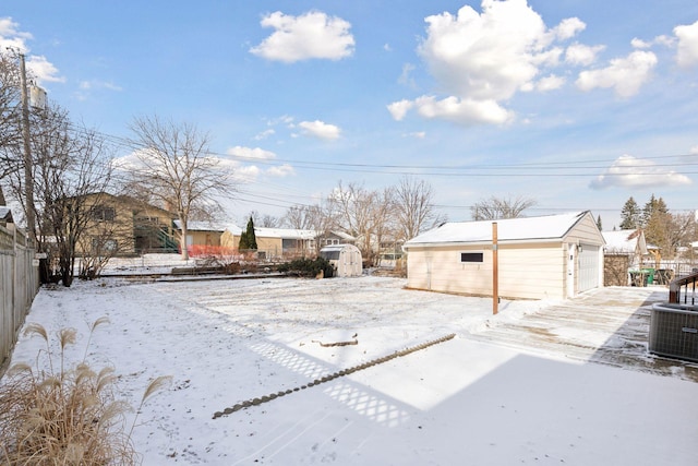 yard layered in snow featuring a garage, an outdoor structure, and central AC unit