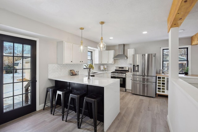 kitchen with wall chimney range hood, appliances with stainless steel finishes, white cabinetry, a kitchen breakfast bar, and kitchen peninsula