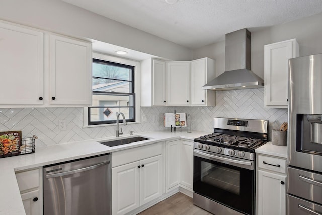 kitchen with wall chimney exhaust hood, sink, stainless steel appliances, decorative backsplash, and white cabinets