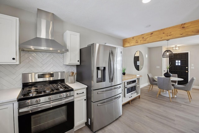 kitchen featuring stainless steel appliances, white cabinetry, tasteful backsplash, and wall chimney range hood