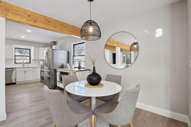 dining space with plenty of natural light, sink, beam ceiling, and light hardwood / wood-style flooring