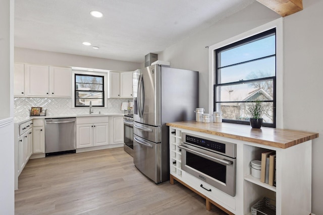 kitchen with sink, appliances with stainless steel finishes, white cabinets, wood counters, and decorative backsplash