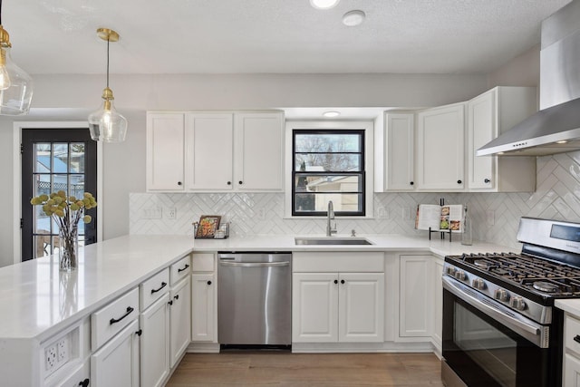 kitchen with wall chimney range hood, appliances with stainless steel finishes, white cabinetry, hanging light fixtures, and kitchen peninsula