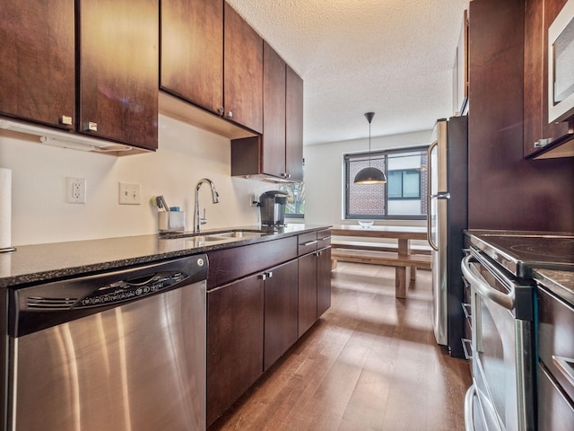 kitchen featuring a textured ceiling, stainless steel appliances, sink, decorative light fixtures, and light hardwood / wood-style floors