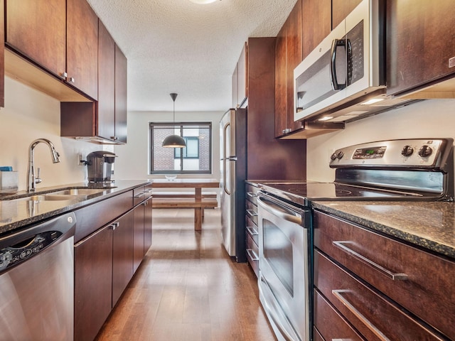 kitchen featuring pendant lighting, sink, light wood-type flooring, a textured ceiling, and appliances with stainless steel finishes