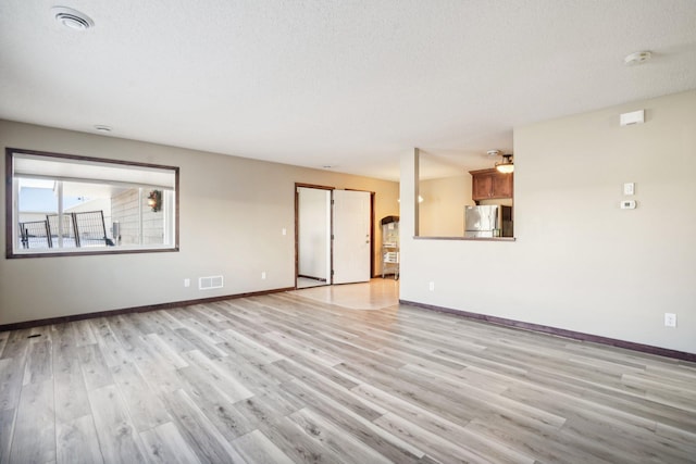 empty room with a textured ceiling and light hardwood / wood-style floors