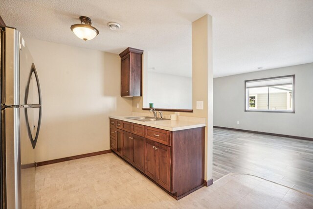 kitchen featuring stainless steel fridge, sink, a textured ceiling, and light wood-type flooring