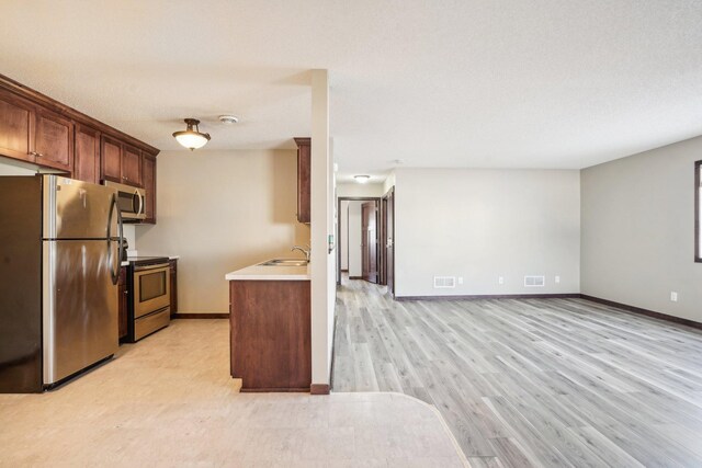 kitchen with a textured ceiling, sink, stainless steel appliances, and light hardwood / wood-style flooring